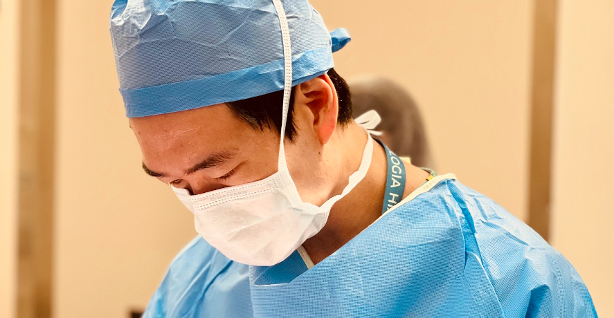 Médico de máscara e roupa cirúrgica realiza procedimento, representando tratamento para próstata aumentada.