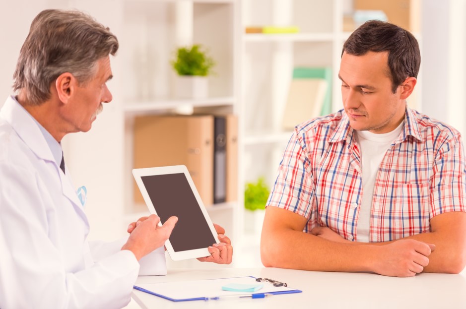 Médico urologista mostrando em seu tablet como funciona o exame de cistoscopia para o seu paciente homem de meia-idade.