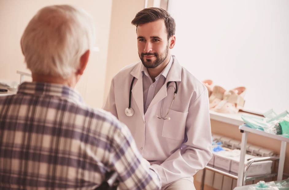 Urologista explicando para paciente idoso sobre hiperplasia prostática benigna, seus sintomas, diagnóstico e tratamentos para próstata aumentada em consulta médica especializada