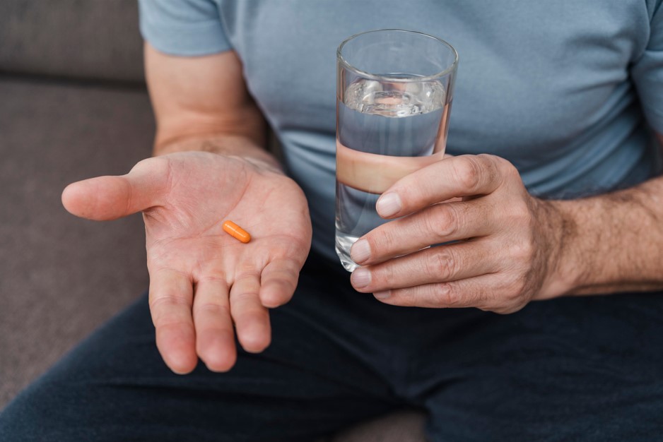 Silhueta de um homem sentado no sofá com um comprimido em mãos tomando um medicamento para disfunção erétil.