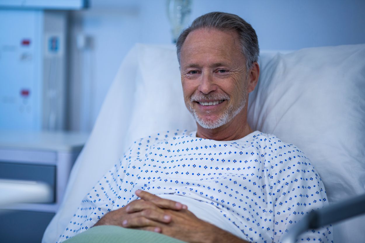 Homem maduro sorrindo em leito hospitalar moderno, representando confiança no tratamento do câncer de próstata.