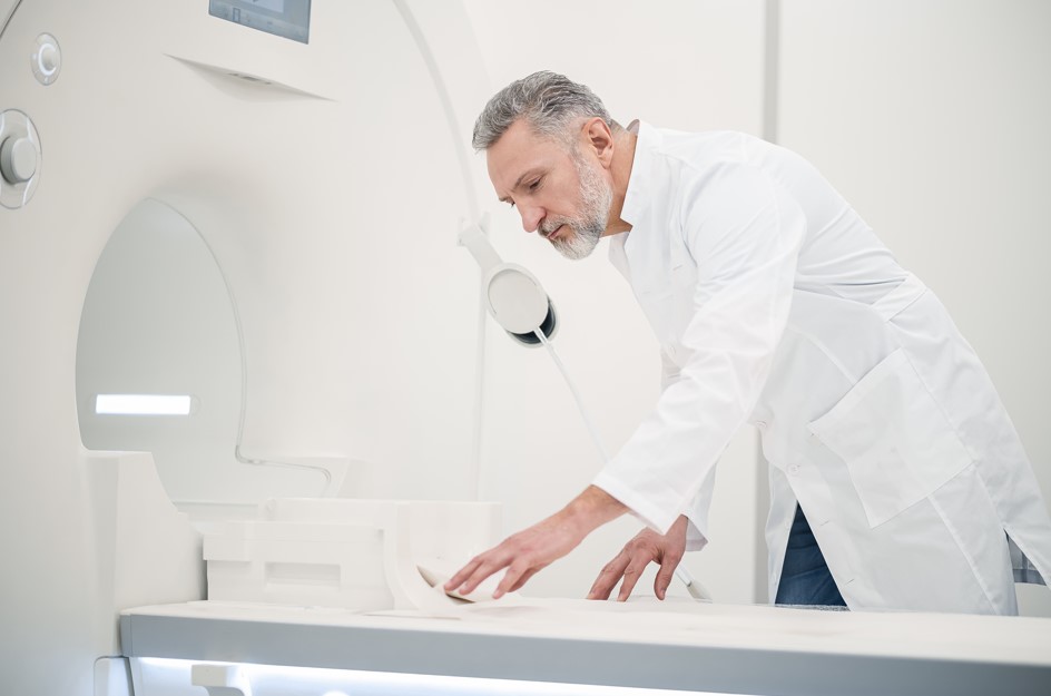 A imagem mostra um médico maduro e experiente preparando um aparelho para um PET Scan, um exame de diagnóstico médico.