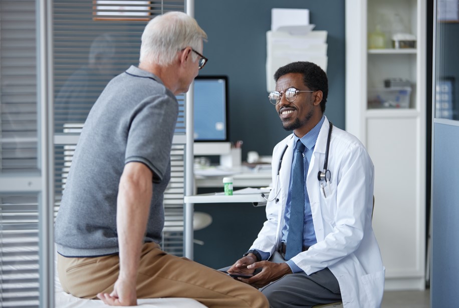 Médico urologista sorridente conversando com um paciente idoso durante uma consulta em um consultório moderno.