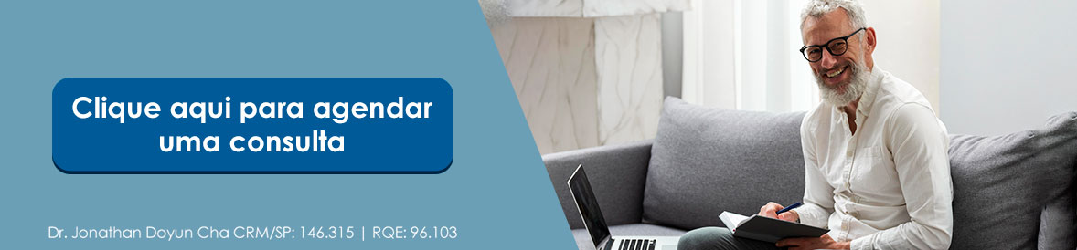 omem maduro sorrindo com laptop no sofá ao lado do botão "Clique aqui para agendar uma consulta" com o Dr. Jonathan Doyun Cha, urologista — CRM/SP: 146.315.