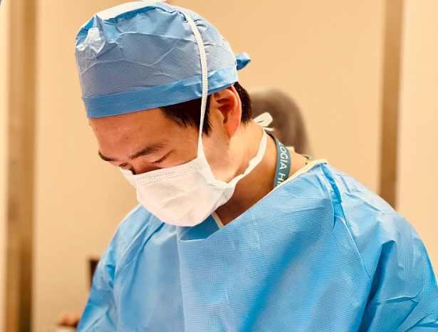 Médico urologista Dr. Jonathan Doyun Cha utilizando roupa cirúrgica e máscara em ambiente hospitalar durante procedimento médico.